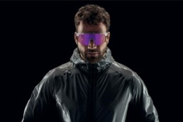 Mann mit reflektierender Jacke und lila getönten Sportsonnenbrillen vor schwarzem Hintergrund