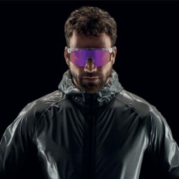 Mann mit reflektierender Jacke und lila getönten Sportsonnenbrillen vor schwarzem Hintergrund