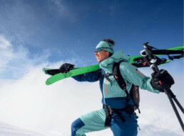 Skifahrer in Skiausruestung traegt Skier und Skistoecke waehrend er durch Schnee geht